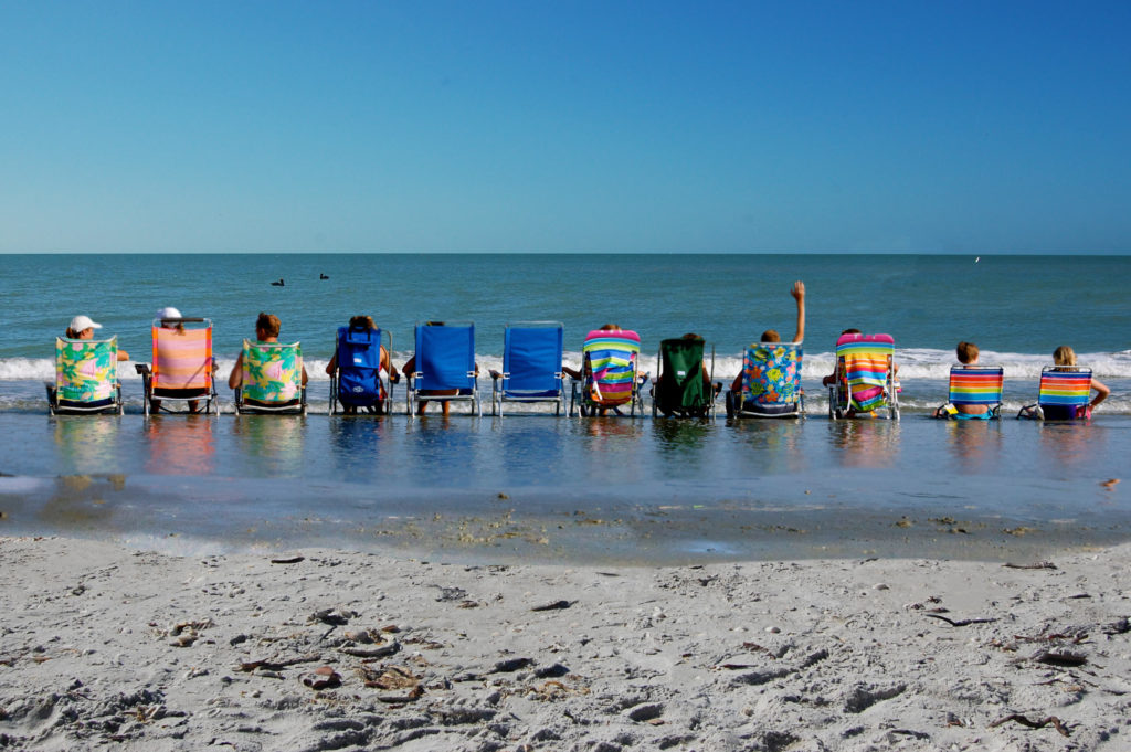 Row of people sitting in their beach chairs letting the waves hit their feet on Sanibel Island