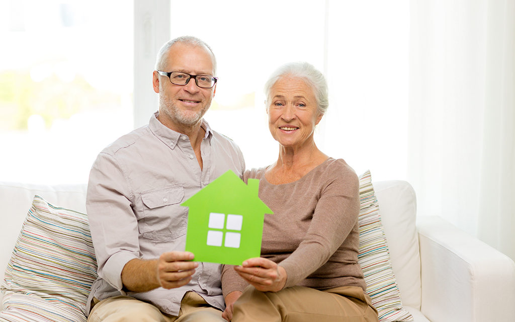 An older couple holding up a cardboard cutout of a home