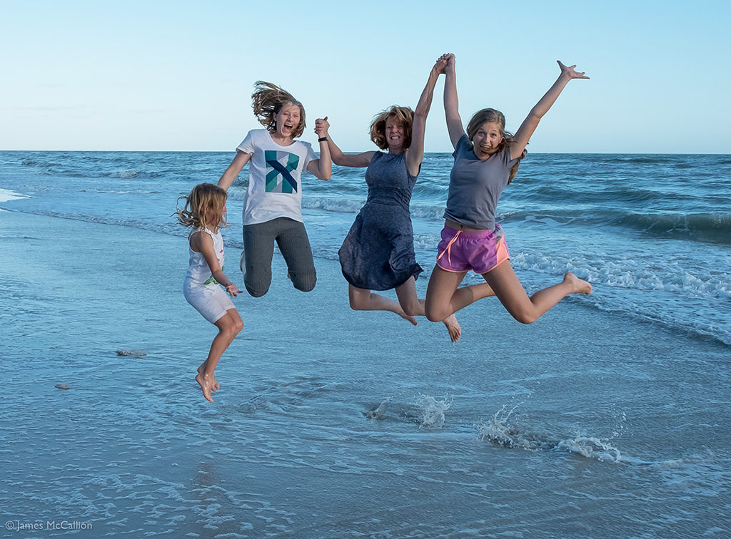 Susan McCallion and her kids holding hands and jumping on the beach on Sanibel Island